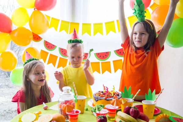 Los niños celebran un cumpleaños. El niño apaga las velas del pastel. Fiesta de frutas . —  Fotos de Stock