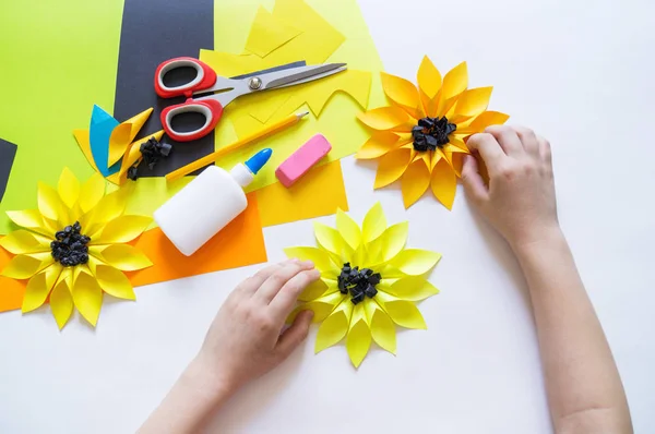 Handen van het kind maakt een oneven bloem papier uit zonnebloem. Gele plant zomer. Het creatieve proces. — Stockfoto