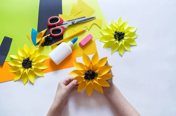 Manos del niño hace un papel de flores extraño de girasol. Planta amarilla verano. El proceso creativo . — Foto de Stock