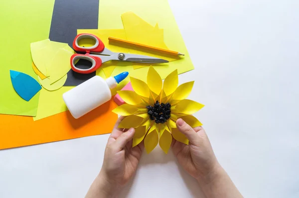 Kezében a gyermek tesz furcsa virágot papírt ki a napraforgó. Sárga növény-nyár. Az alkotási folyamat. — Stock Fotó
