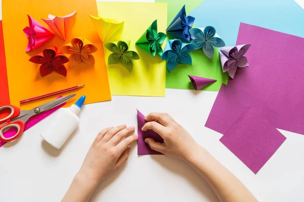 Hands of the girl origami puts flowers from paper of Violet trend color. Lesson of origami. Flat lay style.