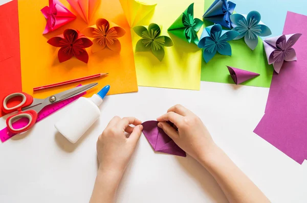 Hands of the girl origami puts flowers from paper of Violet trend color. Lesson of origami. Flat lay style.