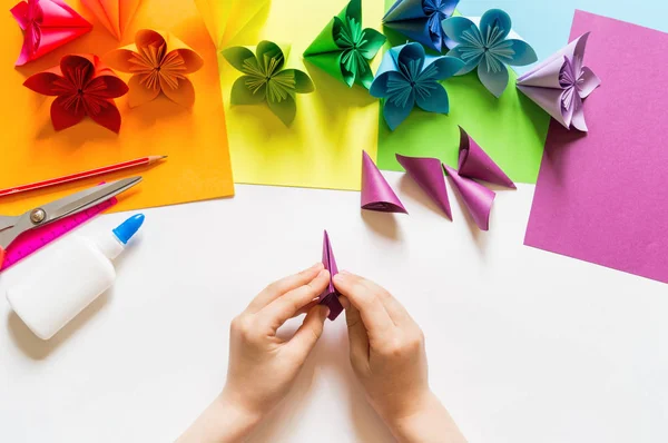 Le mani dell'origami di ragazza mettono fiori di carta di colore di tendenza viola. Lezione di origami. Stile flat lay . — Foto Stock