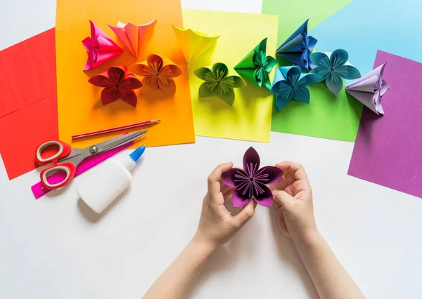 Le mani dell'origami di ragazza mettono fiori di carta di colore di tendenza viola. Lezione di origami. Stile flat lay . — Foto Stock