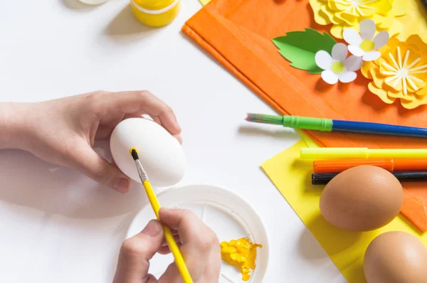 Gyermek kezek lány fest egy húsvéti tojást. Tojás egy sárga méh. Fehér háttér. Anyag kreativitásért, — Stock Fotó