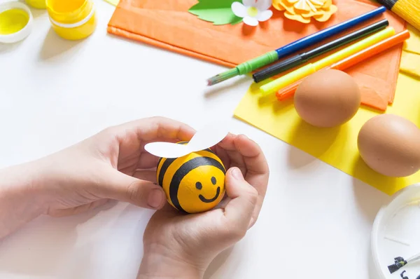 Дитячі руки дівчина малює пасхальне яйце. Яйце жовта бджола. Білий фон. Матеріал для творчості , — стокове фото