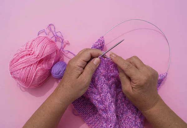 As mãos da mulher tricotam um gorro de fio roxo. Fundo rosa — Fotografia de Stock