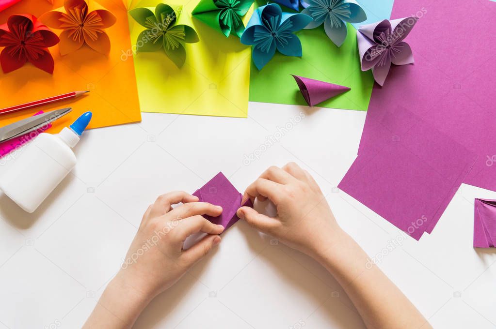 Hands of the girl origami puts flowers from paper of Violet trend color. Lesson of origami. Flat lay style.