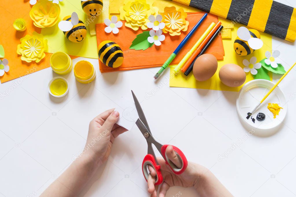 Child hands girl paints an Easter egg. Egg a yellow bee. White background. Material for creativity,