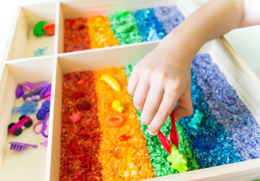 İçinde gökkuşağı pirinci olan duyusal kutu. Montessori materyali bebek