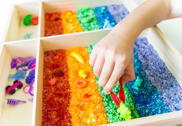 İçinde gökkuşağı pirinci olan duyusal kutu. Montessori materyali bebek