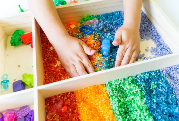 İçinde gökkuşağı pirinci olan duyusal kutu. Montessori materyali bebek