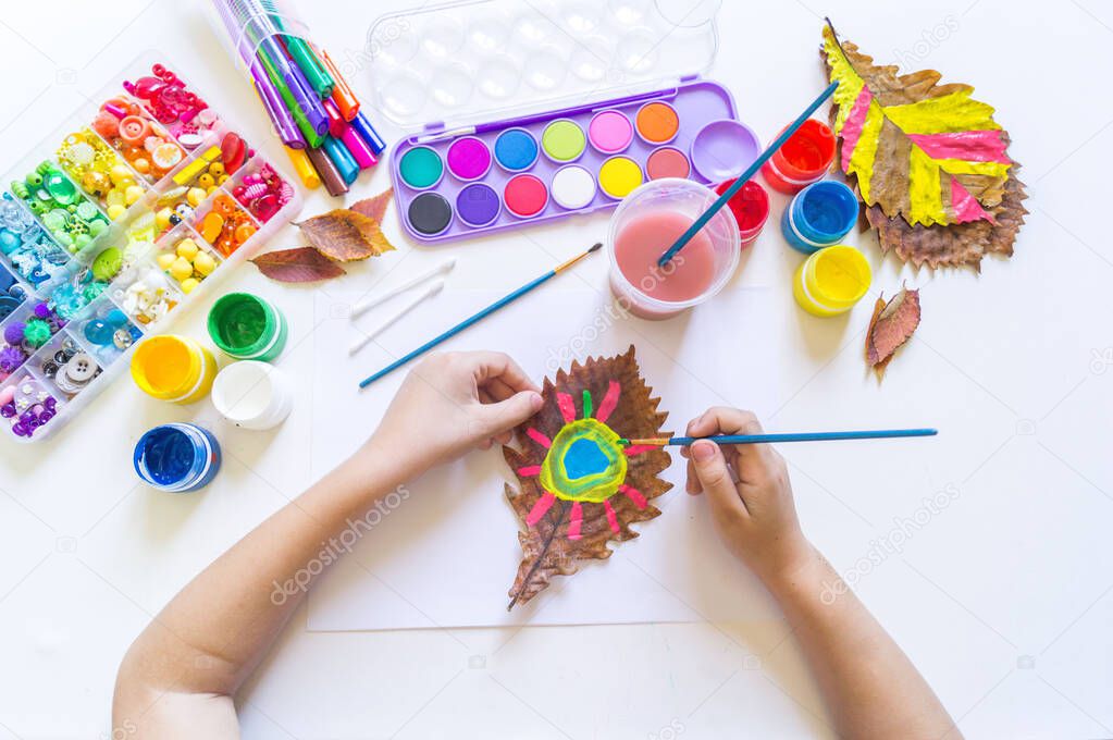 child draws on an autumn leaf.