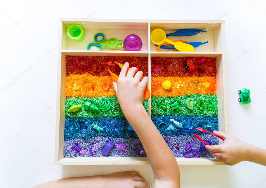 Sensory box with rainbow rice inside. Montessori material baby