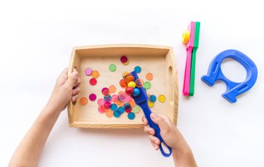 Montessori mıknatısı düz yerde yatıyordu. Çocuklar el muamelesi görür. Beyaz arkaplanda tahta tepsi.