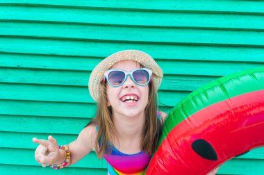Şişme karpuzlu bir kız. Ahşap yeşil arka plan. Plaj havuzunda ailenle aktif tatiller. Duygusal çocuk.