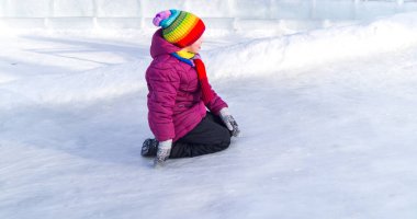 Kız karda debeleniyor. Tepeden düştü. Mutlu kış sporları ailesi. Parlak elbiseler gökkuşağı şapkası.