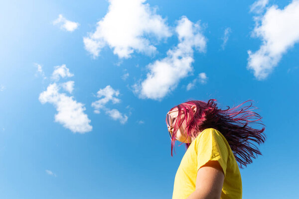 Attractive young girl with pink hair is dancing. Sky background with clouds. Party and fun concept. Kid hair magnificent