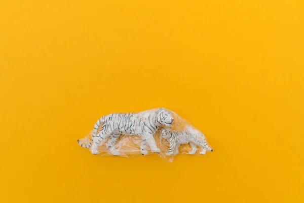 Tiger is entangled in a plastic bag. Plastic animal concept. Yellow background. Environmental pollution problem.