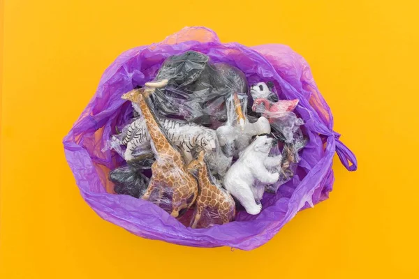 Many plastic animals are in a purple bag. Plastic animal concept. Yellow background. Environmental pollution problem.