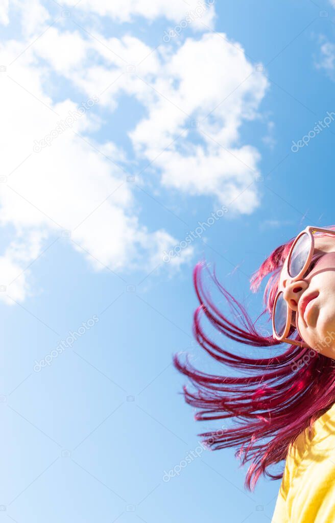Attractive young girl with pink hair is dancing. Sky background with clouds. Party and fun concept. Kid hair magnificent