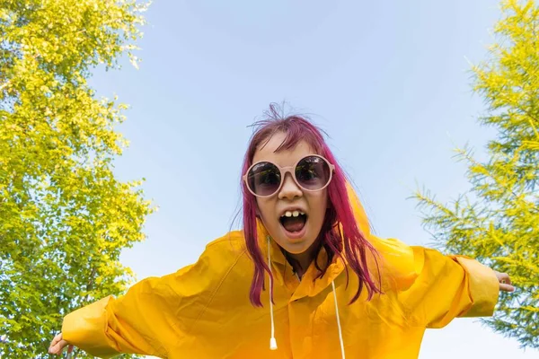 Girl in a yellow raincoat. Summer walk. Blue sky background. Hipster teenager having fun and looking at the camera
