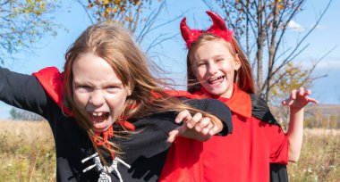 Cadılar Bayramı kostümlü kız arkadaşlar oynuyor. Açık alan. Şeytan ve cadı gibi giyinmiş gizemli bir ortam.