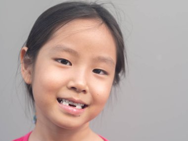 Asyalı küçük şirin kız gülümseme kırık diş ile gri backgr