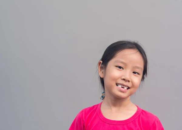 Asian little cute girl smile with her broken tooth, grey backgr — стоковое фото