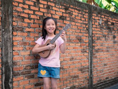 Küçük Asyalı çocuk oynamak ukulele, eski tuğla duvar arka plan