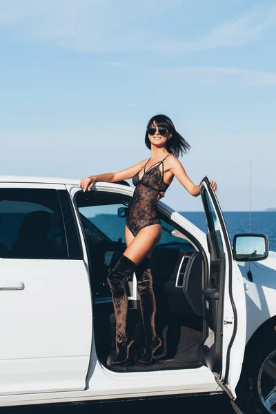Ragazza sexy in lingerie si trova su una macchina bianca con una porta aperta su uno sfondo di acqua e cielo — Foto Stock