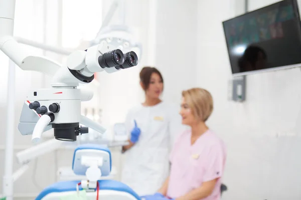 Microscopio binocular endodóntico dental profesional en la sala de tratamiento. En el contexto de dos dentistas. Enfoque en el microscopio — Foto de Stock