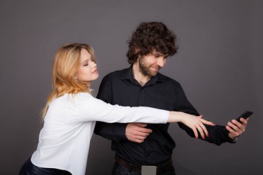 bir adamdan bir telefon almaya çalışan bir genç kadın. Studio gri bir arka plan üzerinde çekilen fotoğraf