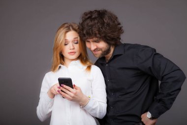 Genç Sarışın kadın ve esmer adam bir akıllı telefon arıyor. Studio gri bir arka plan üzerinde çekilen fotoğraf