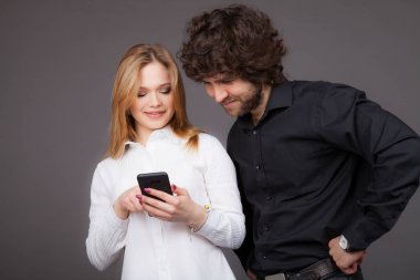 Genç Sarışın kadın ve esmer adam bir akıllı telefon arıyor. Studio gri bir arka plan üzerinde çekilen fotoğraf