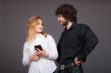 Genç Sarışın kadın ve birbirine bakarak esmer bir adam. Bir kadın bir smartphone tutuyor. Studio gri bir arka plan üzerinde çekilen fotoğraf