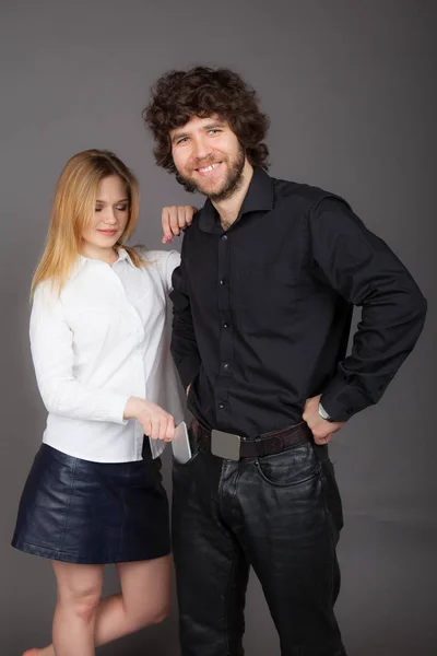 a young blonde woman pulls the phone out of her pocket for a brunette man. Photo taken in studio on a gray background