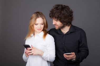 Genç Sarışın kadın ve kıvırcık saçlı esmer adam kendi smartphones içinde arıyor. Stüdyo tarafından çekilen fotoğraflar