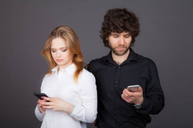 Genç Sarışın kadın ve kıvırcık saçlı esmer adam kendi smartphones içinde arıyor. Stüdyo tarafından çekilen fotoğraflar