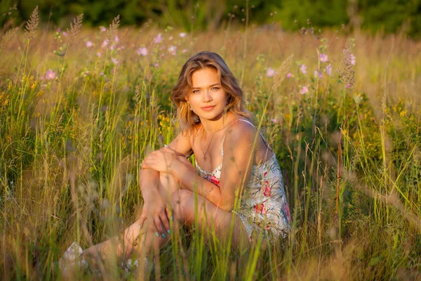 Mulher bonita sentada no campo, grama verde e flores. Ao ar livre Desfrute da natureza. Menina sorrindo saudável sentado na grama verde — Fotografia de Stock