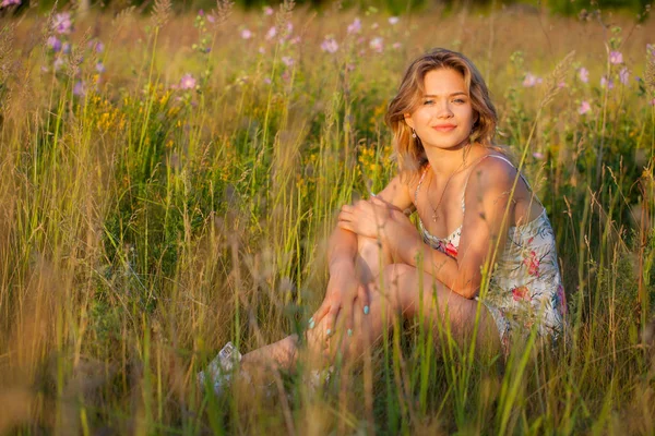 Красива молода жінка сидить на полі, зелена трава і квіти. Насолоджуйтесь природою на відкритому повітрі. Здорова усміхнена дівчина сидить у зеленій траві — стокове фото
