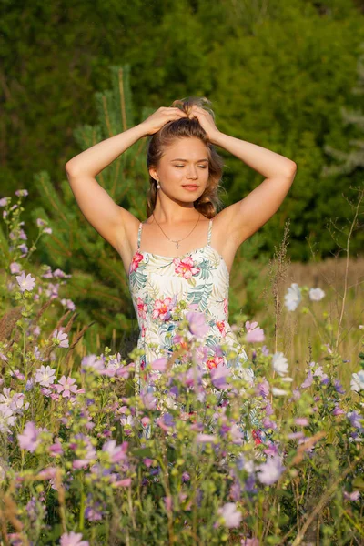 Mulher bonita em pé em um campo, grama verde e flores. Ao ar livre Desfrute da natureza. Menina sorrindo saudável em pé na grama alta — Fotografia de Stock