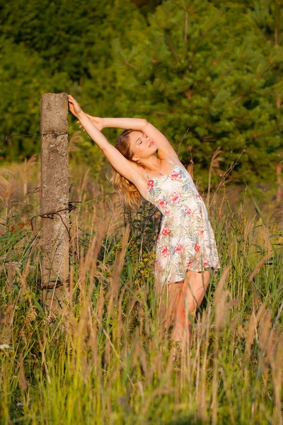 Mulher bonita em pé em um campo perto de um pilar de concreto, grama verde e flores. Ao ar livre Desfrute da natureza. Menina sorrindo saudável em pé na grama alta — Fotografia de Stock