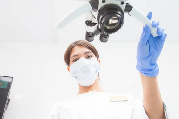 Microscopio binocular endodóntico dental profesional en una sala de tratamiento Una doctora observa la cámara. Vista inferior — Foto de Stock