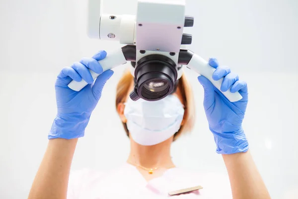 Μια γυναίκα οδοντίατρος εξετάζει ένα οδοντιατρικό μικροσκόπιο. Κάτω όψη. Επικεντρωθείτε στο μικροσκόπιο — Φωτογραφία Αρχείου