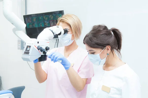 Microscopio binoculare professionale, due dentiste guardano la paziente con maschere mediche — Foto Stock