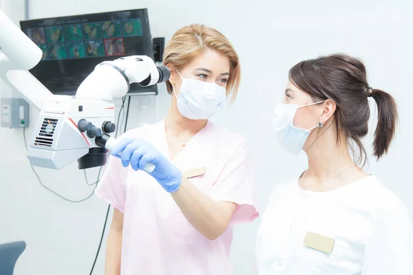 Microscope binoculaire dentaire professionnel, deux dentistes féminines se regardent, dans des masques médicaux — Photo