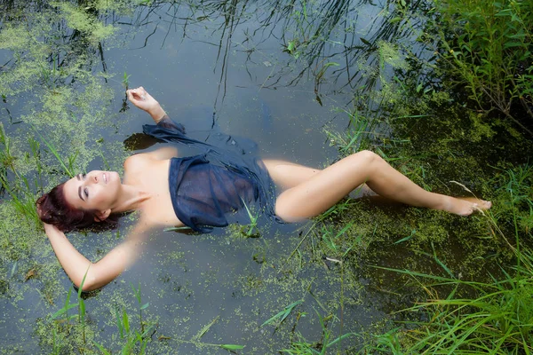 Uma jovem mulher jaz em um pântano coberto com um pano preto — Fotografia de Stock