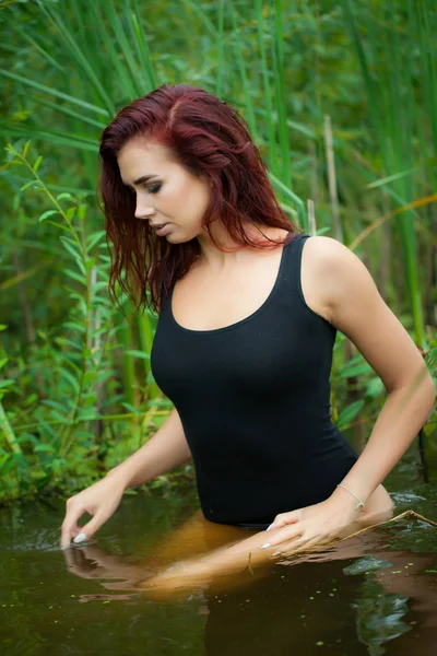 Красива молода сексуальна жінка сидить у воді в чорному купальнику, на фоні кросівки — стокове фото