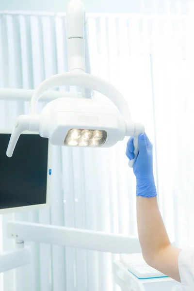 Mano del dentista sosteniendo la lámpara en la clínica de un dentista con camino — Foto de Stock